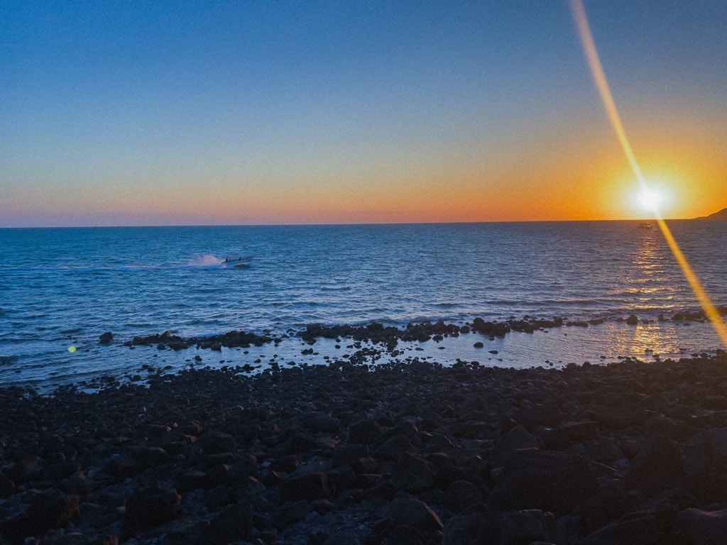 Atardecer sobre el Mar de Cortés desde la costa rocosa de Puerto Peñasco, con una panga navegando cerca de la orilla